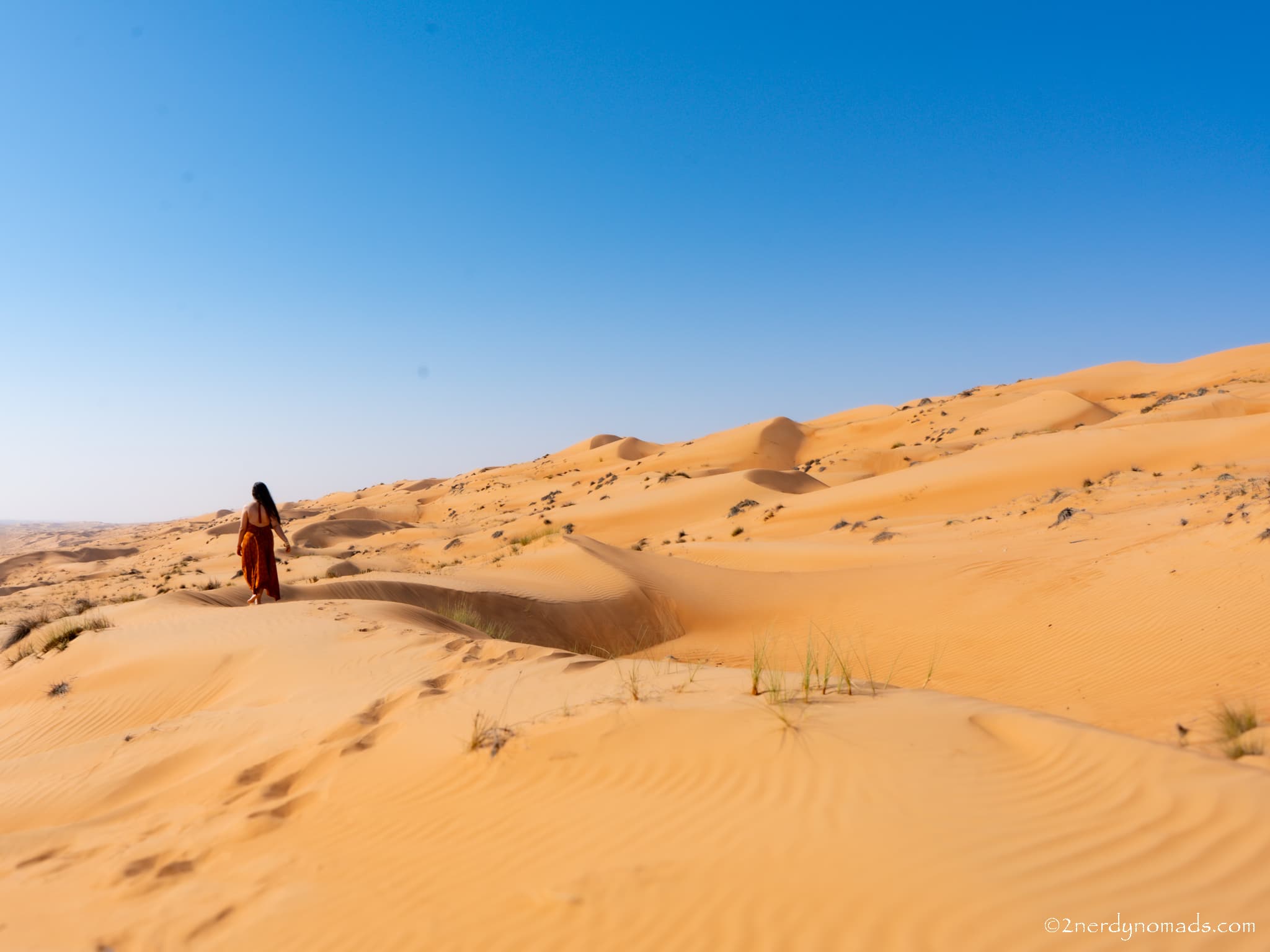 Urvi walking across the golden sand dunes of Wahiba Sands in Oman during a two-week Oman road trip.