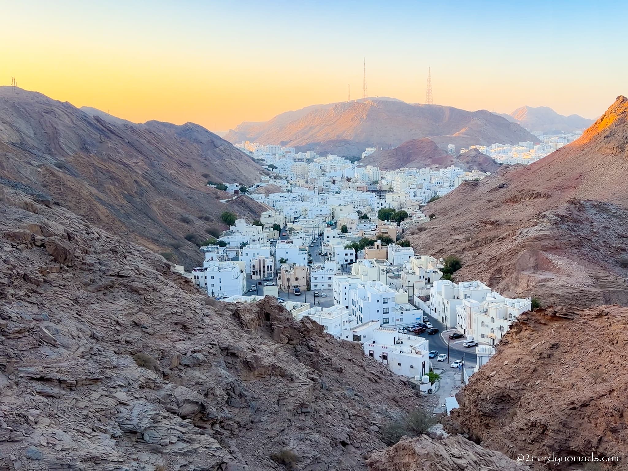 White houses nestled between rugged mountains at Yiti Viewpoint near Muscat, Oman, during sunset.