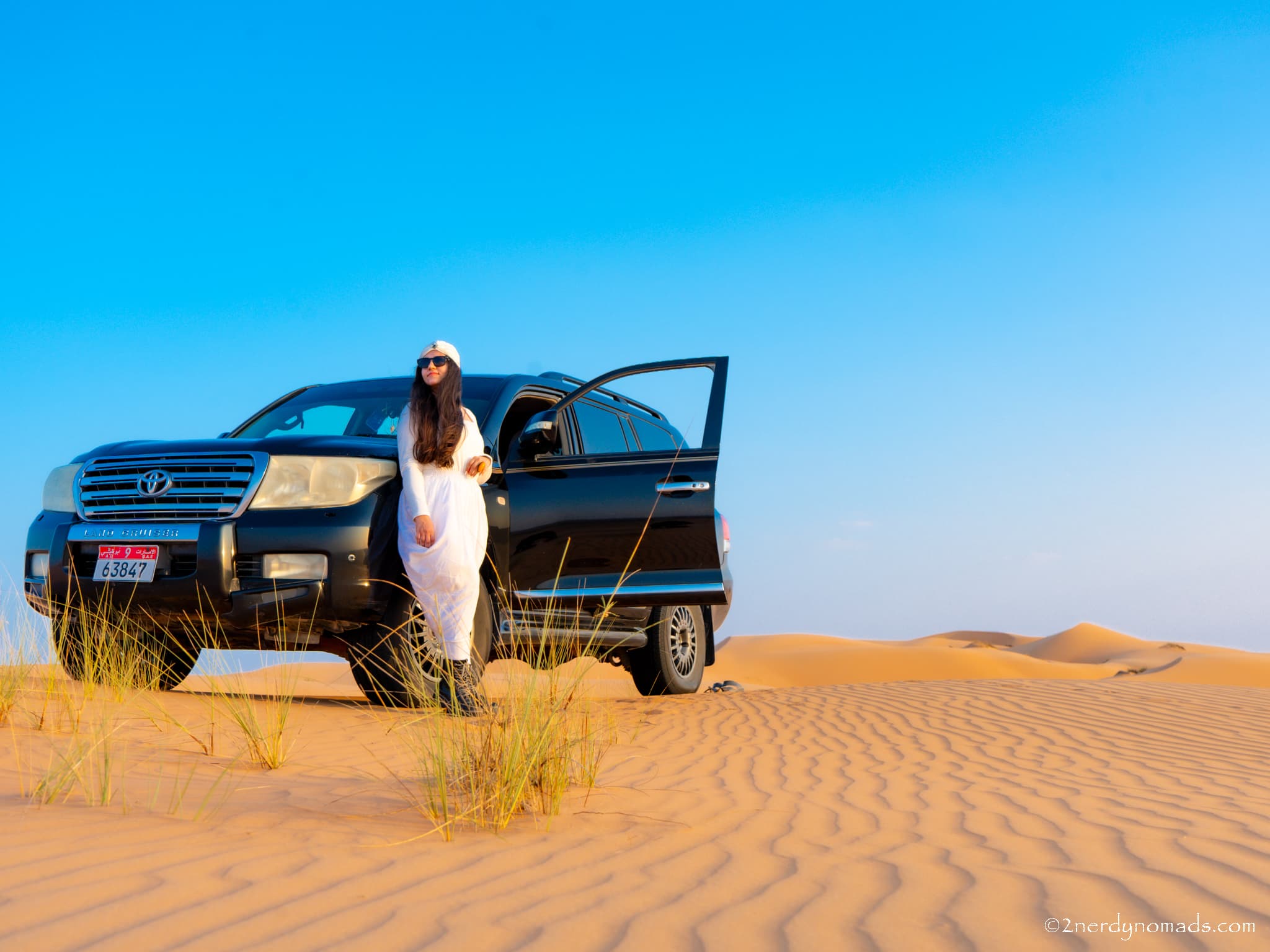 Urvi standing beside a 4x4 vehicle in the sand dunes of Wahiba Sands, Oman, during a road trip.